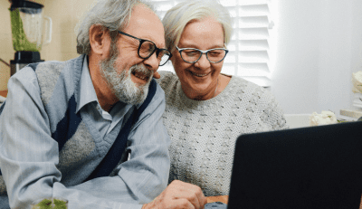 Elderly couple smiling and looking at a laptop screen, possibly checking their My TSP account together.
