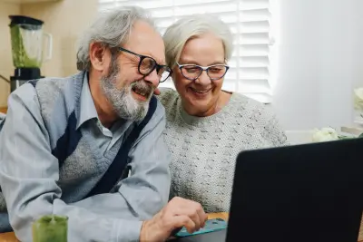 Elderly couple smiling and looking at a laptop screen, possibly checking their My TSP account together.