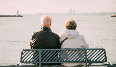 Two individuals seated on a bench overlooking a calm sea, contemplating the horizon, symbolizing planning to calculate retirement.