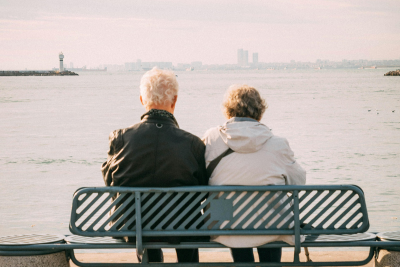 Two individuals seated on a bench overlooking a calm sea, contemplating the horizon, symbolizing planning to calculate retirement.