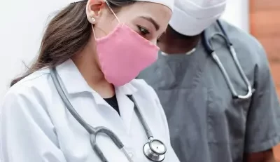 Healthcare professionals in white lab coats with stethoscopes, one with an obscured face and the other wearing a surgical mask.
