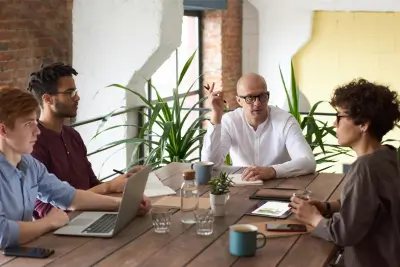 A group of four professionals in a meeting, discussing employee benefit trust, with laptops and documents on the table.