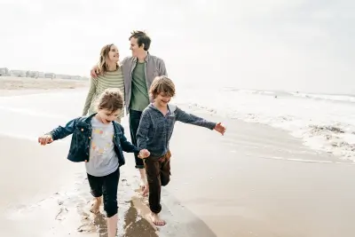 A family of four holding hands and walking along the beach, symbolizing the protection and long-term benefits of whole life insurance.
