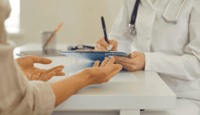 A healthcare professional in a white coat is taking notes on a clipboard while listening to a patient, highlighting the importance of employee benefits health.