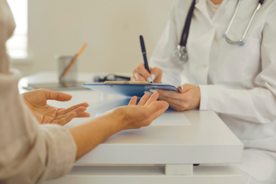 A healthcare professional in a white coat is taking notes on a clipboard while listening to a patient, highlighting the importance of employee benefits health.