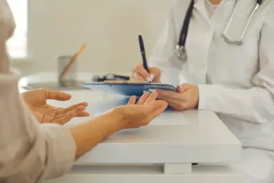 A healthcare professional in a white coat is taking notes on a clipboard while listening to a patient, highlighting the importance of employee benefits health.
