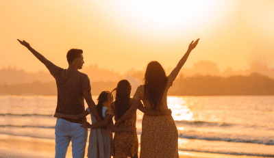A family of four, with two adults and two children, stands on a beach at sunset, raising their arms in a gesture of joy and freedom, symbolizing the benefits of work-life balance.