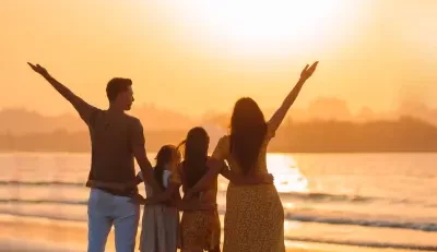 A family of four, with two adults and two children, stands on a beach at sunset, raising their arms in a gesture of joy and freedom, symbolizing the benefits of work-life balance.