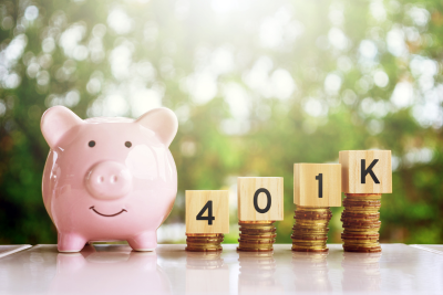 Pink piggy bank and ‘401K’ spelled with wooden blocks on ascending coin stacks, symbolizing the growth of 401(k) benefits.