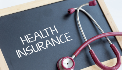 A stethoscope with red tubing rests on a blackboard displaying the words ‘HEALTH INSURANCE’ written in white chalk