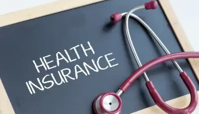 A stethoscope with red tubing rests on a blackboard displaying the words ‘HEALTH INSURANCE’ written in white chalk