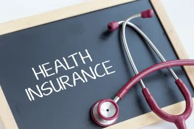 A stethoscope with red tubing rests on a blackboard displaying the words ‘HEALTH INSURANCE’ written in white chalk