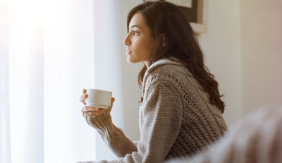 Woman gazing out window with coffee, thinking about life insurance how much do I need.