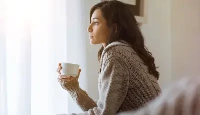 Woman gazing out window with coffee, thinking about life insurance how much do I need.