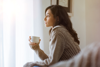 Woman gazing out window with coffee, thinking about life insurance how much do I need.