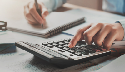 Hands using a calculator and writing notes on financial documents related to the TSP C Fund.