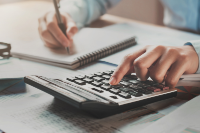 Hands using a calculator and writing notes on financial documents related to the TSP C Fund.